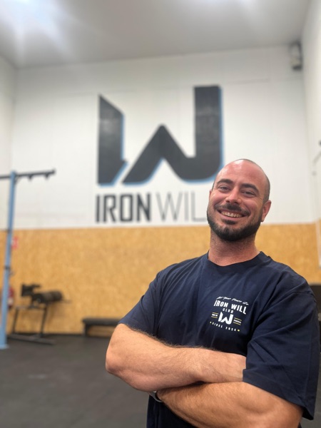 Ribe, head coach y fundador de Iron Will Box, con el logo del box de fondo